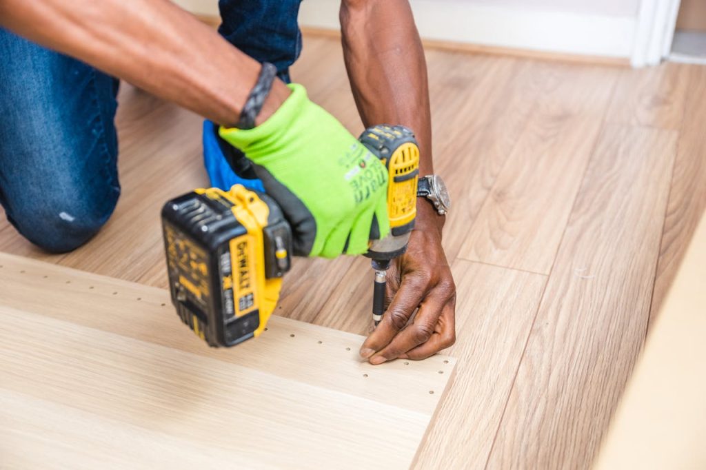 pexels-photo-1249610 Close-up of handyman drilling wood indoors with green gloves and cordless drill.